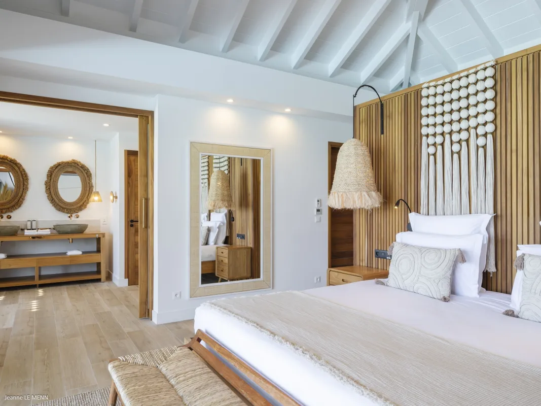 Villa Abaca: Bedroom with wooden wall paneling, woven bench, and ensuite bathroom visible through the doorway