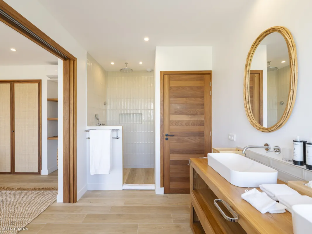 Villa Abaca: Modern bathroom with wooden vanity, oval mirror, and walk-in shower with light tiles