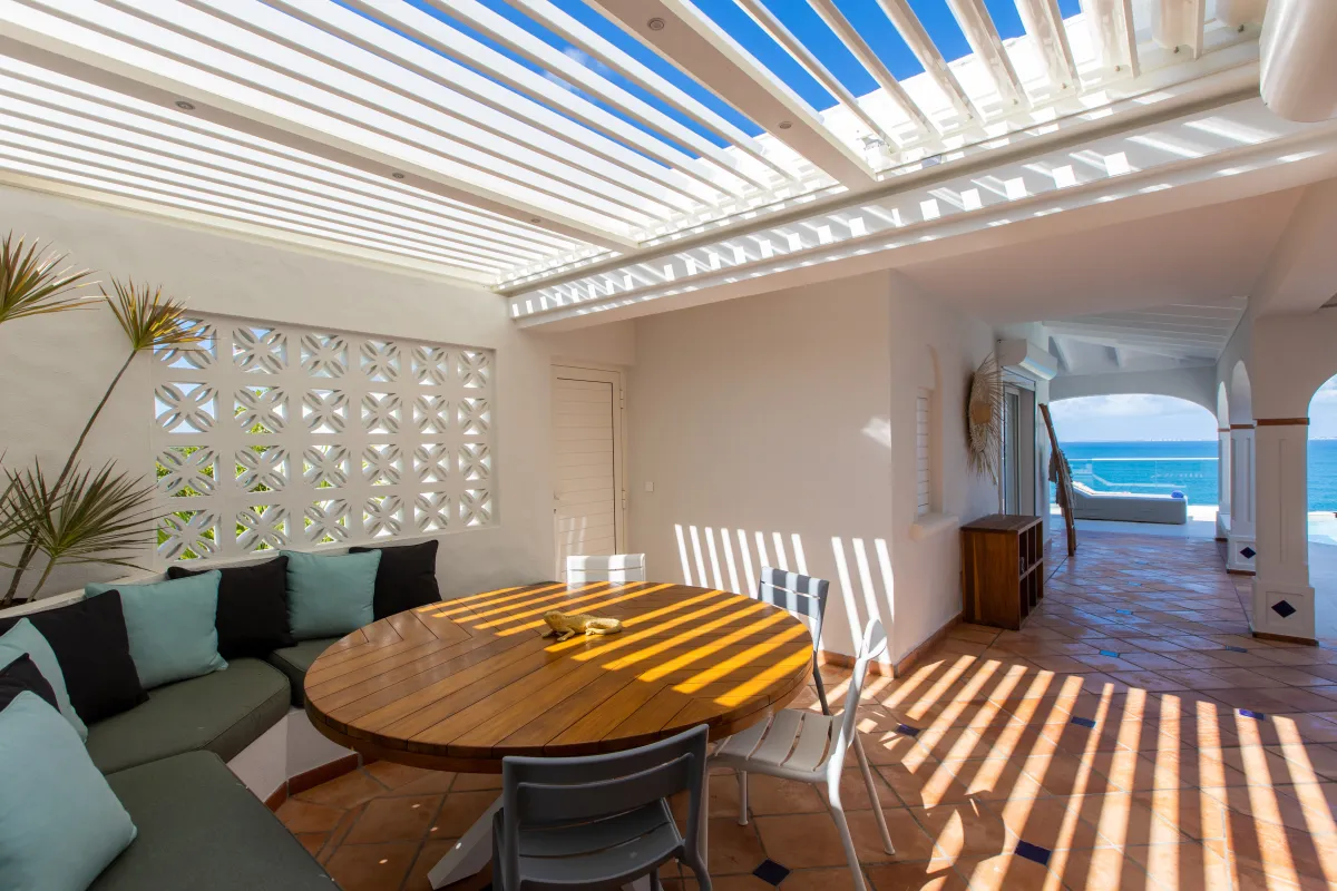 Villa Agama: Covered terrace with a round wooden dining table, built-in banquette, pergola roof, and ocean view
