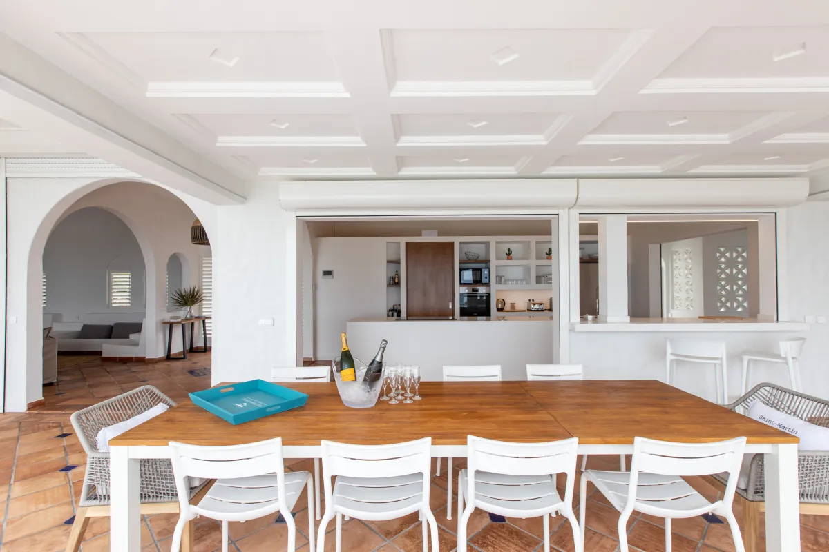 Villa Agama: Long wooden dining table with white chairs on a covered terrace facing an open kitchen