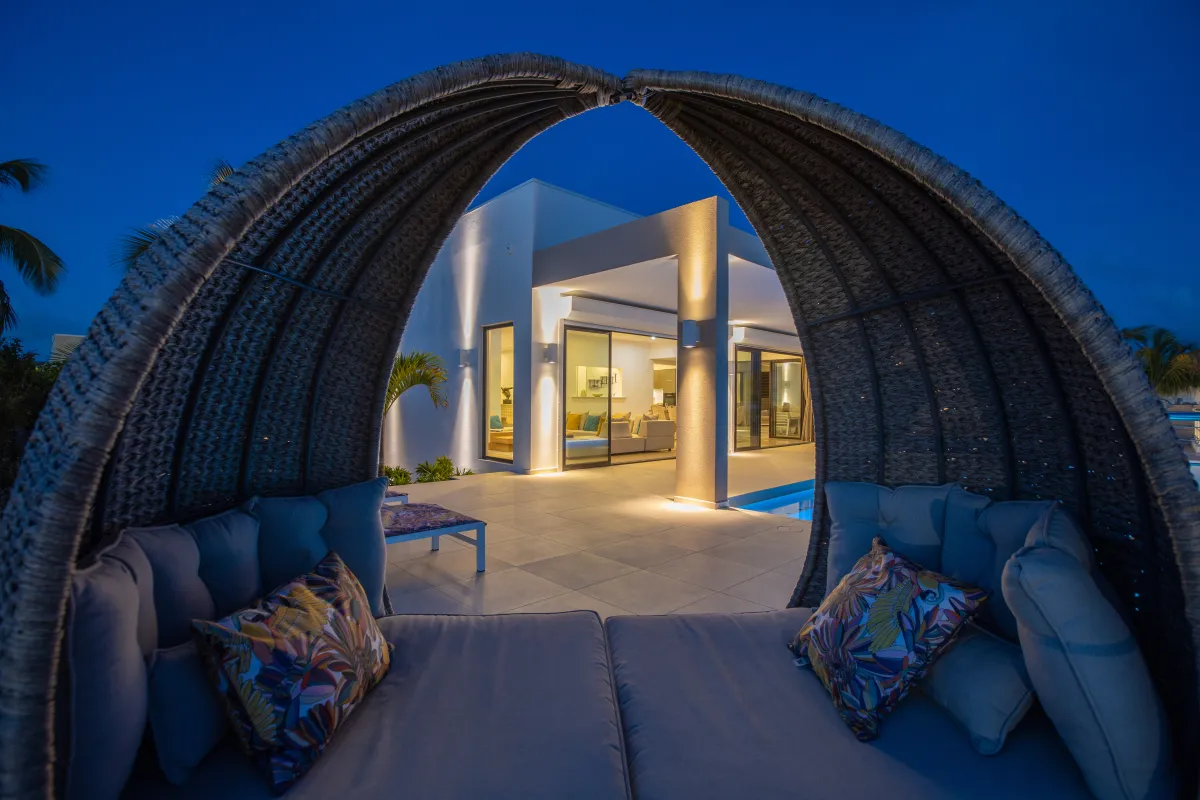 Villa Alma: Covered outdoor daybed on a terrace framing an illuminated modern villa at twilight