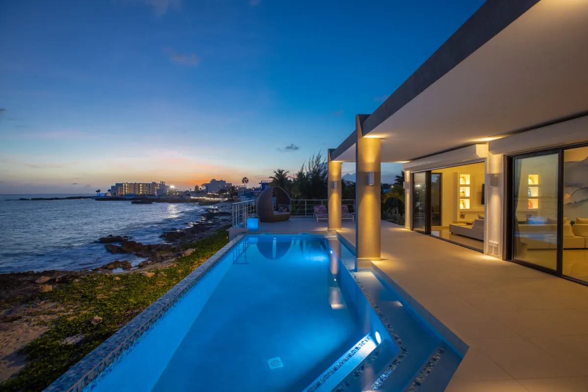 Villa Alma: Illuminated swimming pool and terrace next to the ocean at dusk