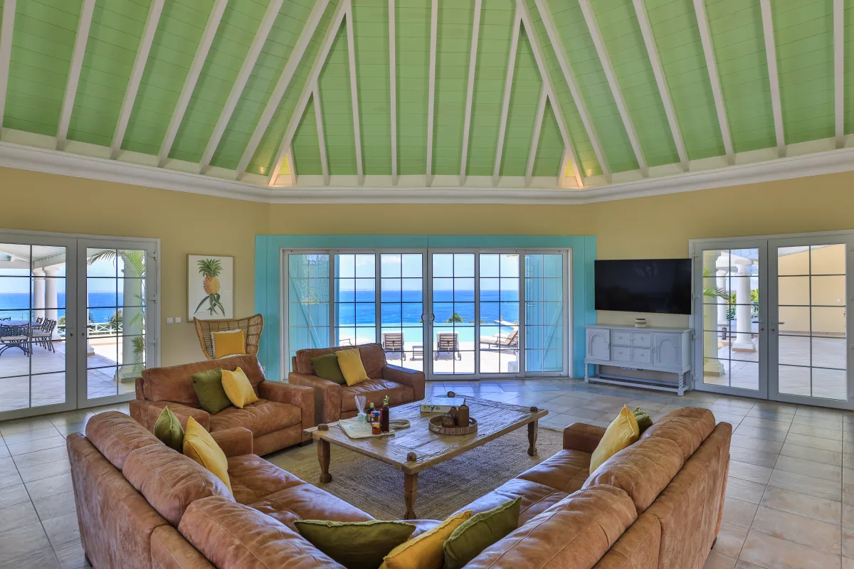Villa Amber: Spacious living room with vaulted ceiling, leather sofas, and ocean views through glass doors