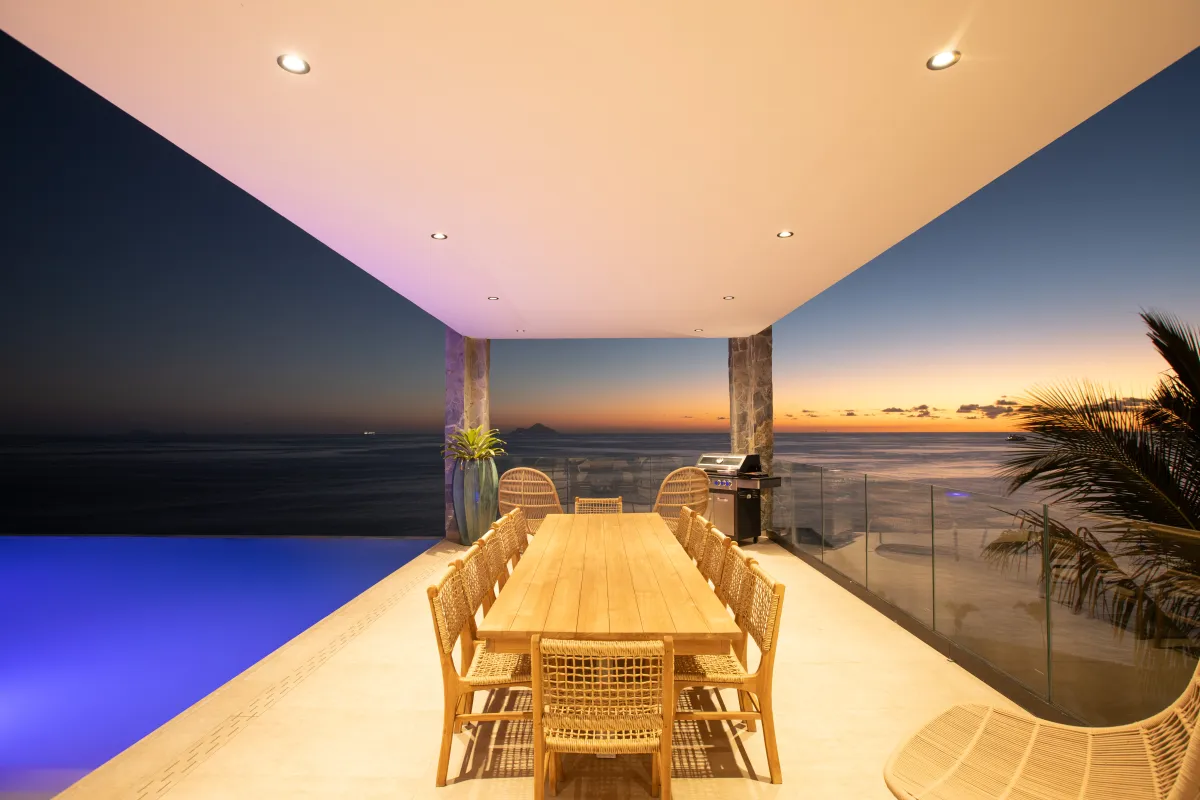 Villa Aqua Dream: Covered terrace with wooden dining table next to an illuminated pool overlooking the sea at sunset