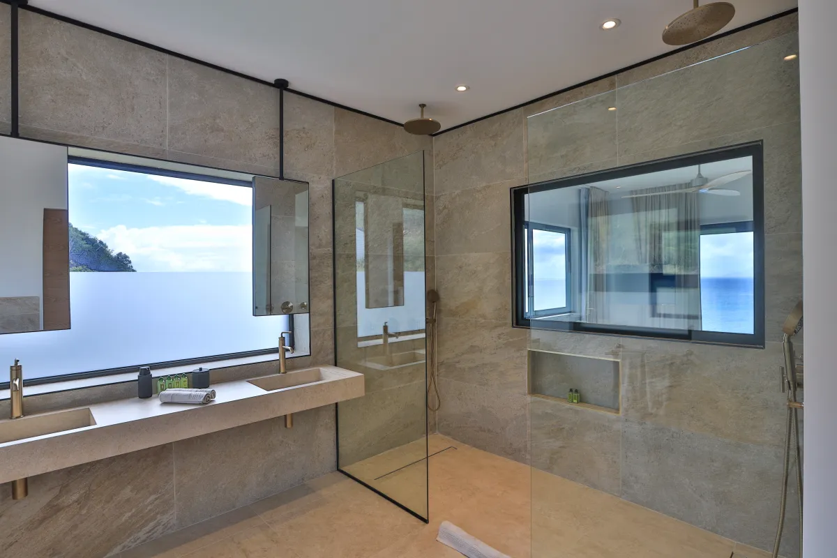Villa Aqua Dream: Modern tiled bathroom with double sink vanity, glass walk-in shower, and window overlooking the sea