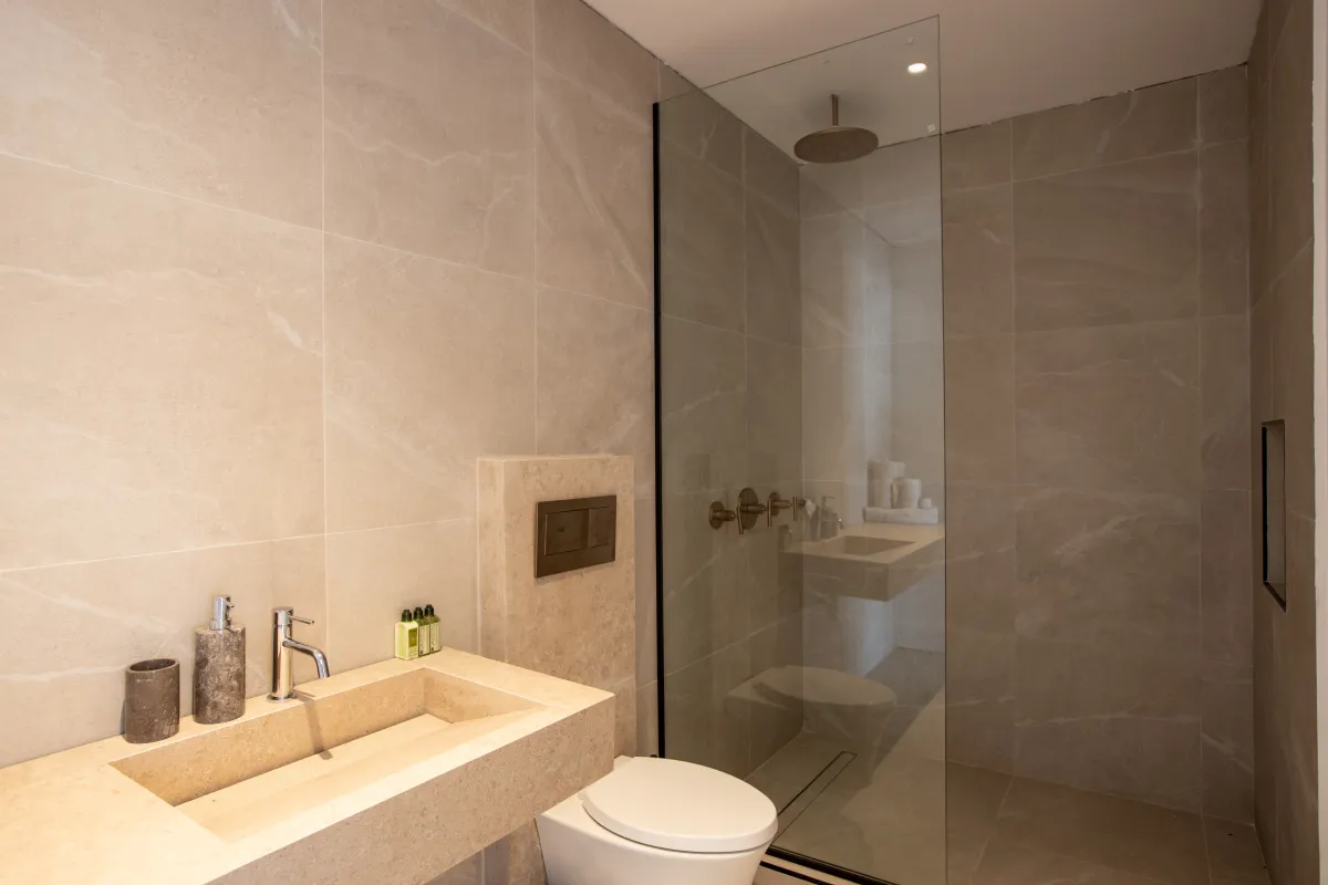 Villa Aqua Dream: Beige stone bathroom with a walk-in glass shower, modern sink, and toilet