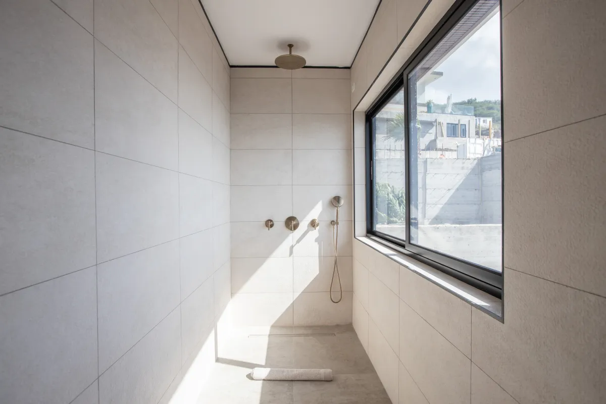 Villa Aqua Vista: Walk-in shower with beige tiles, brass fixtures, and a large window