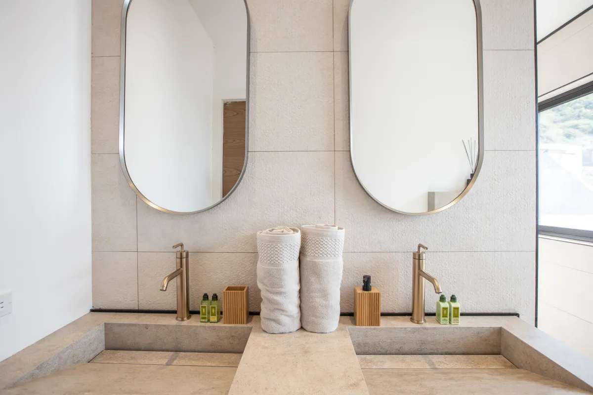 Villa Aqua Vista: Double vanity bathroom with stone integrated sinks, gold fixtures, and two oval mirrors