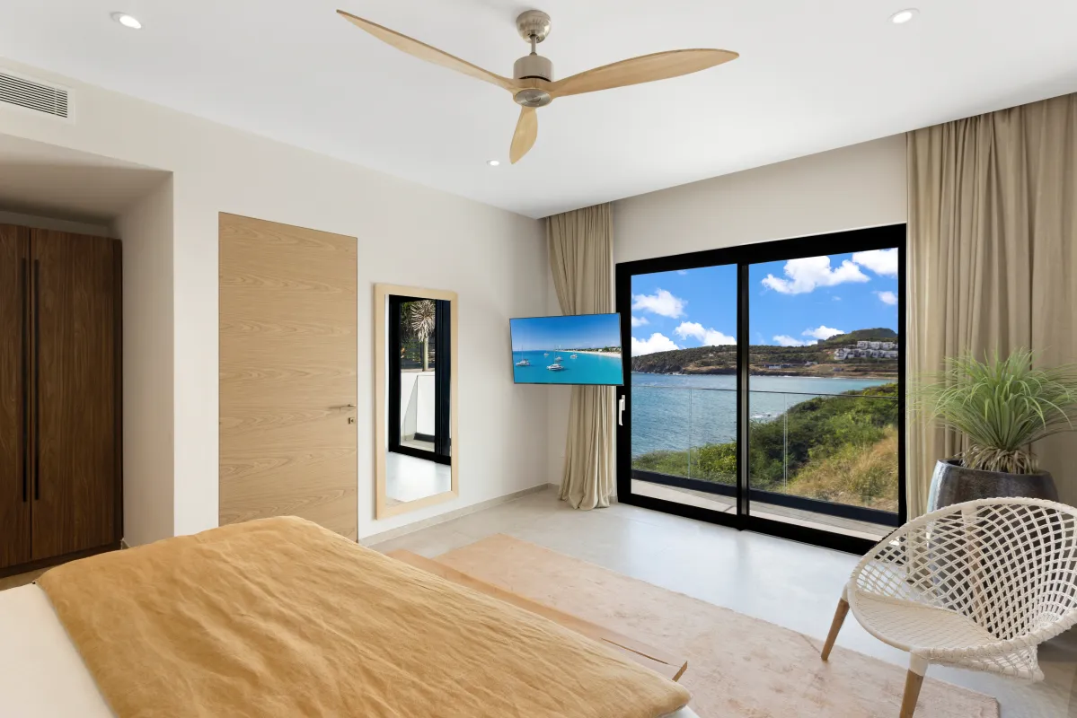 Villa Aqua Vista: Bedroom with sliding glass doors framing an ocean view and a ceiling fan