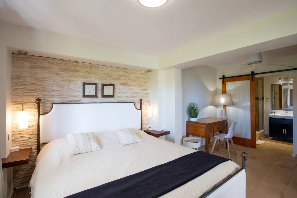 Villa Azur Dream: Bedroom with large bed, textured stone accent wall, and view into the ensuite bathroom