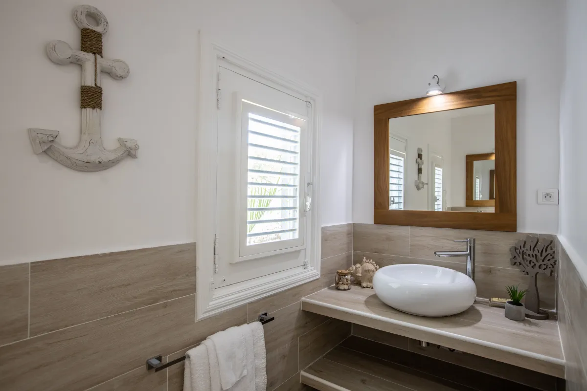 Villa Azur Dream: Bathroom vanity with a round vessel sink, wood-framed mirror, and nautical anchor wall decor