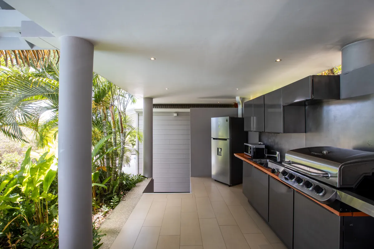 Villa Bahia Blue: Covered outdoor kitchen with modern cabinets, barbecue grill, and refrigerator next to tropical plants