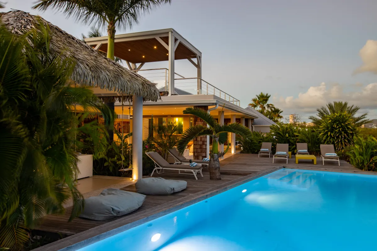 Villa Bahia Blue: Illuminated swimming pool and wooden sun deck beside a tropical villa at dusk