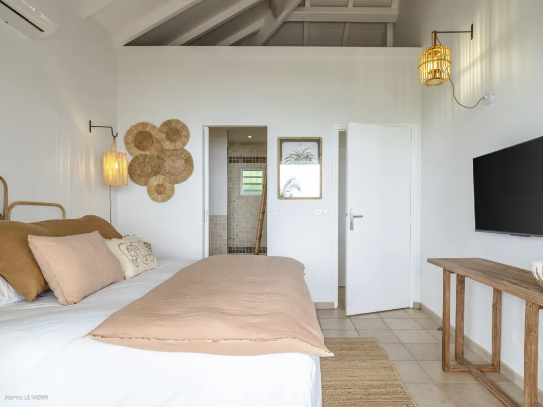 Villa Be Happy: Bedroom with made bed, wall sconces, television, and open doorway to an ensuite bathroom
