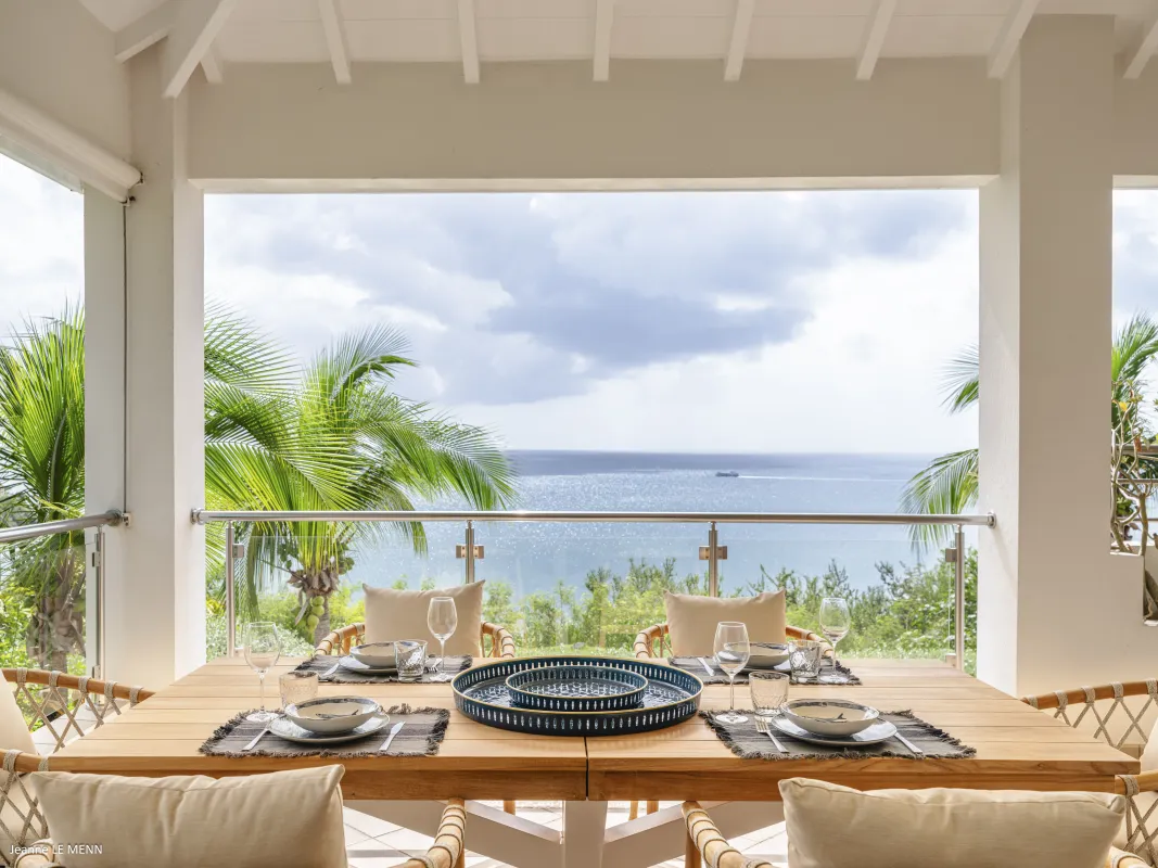 Villa Be Happy: Outdoor dining table set on a covered terrace overlooking palm trees and the ocean