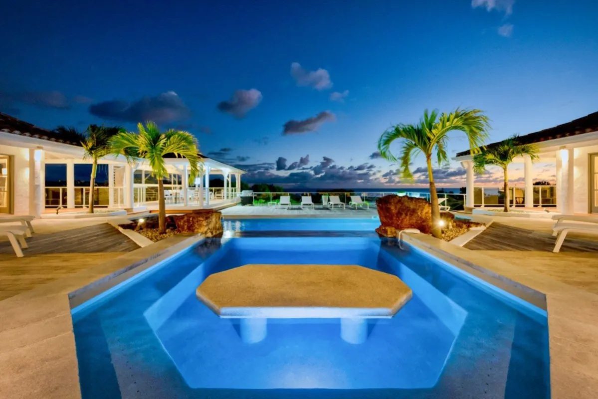 Villa Belle Fontaine: Swimming pool with submerged seating and table overlooking the ocean at dusk