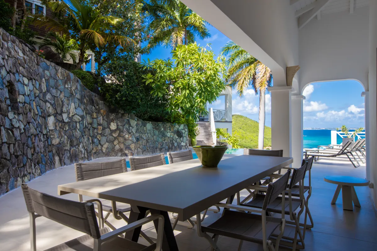 Villa Casa Sand: Covered terrace dining table overlooking a swimming pool, lush greenery, and the ocean