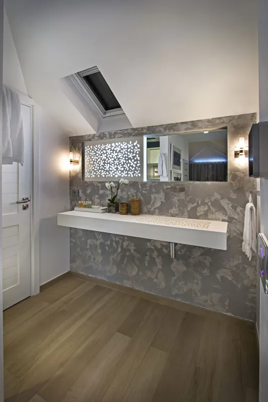 Villa C'est la Vie: Modern bathroom with floating vanity, textured accent wall, mirror, and angled skylight