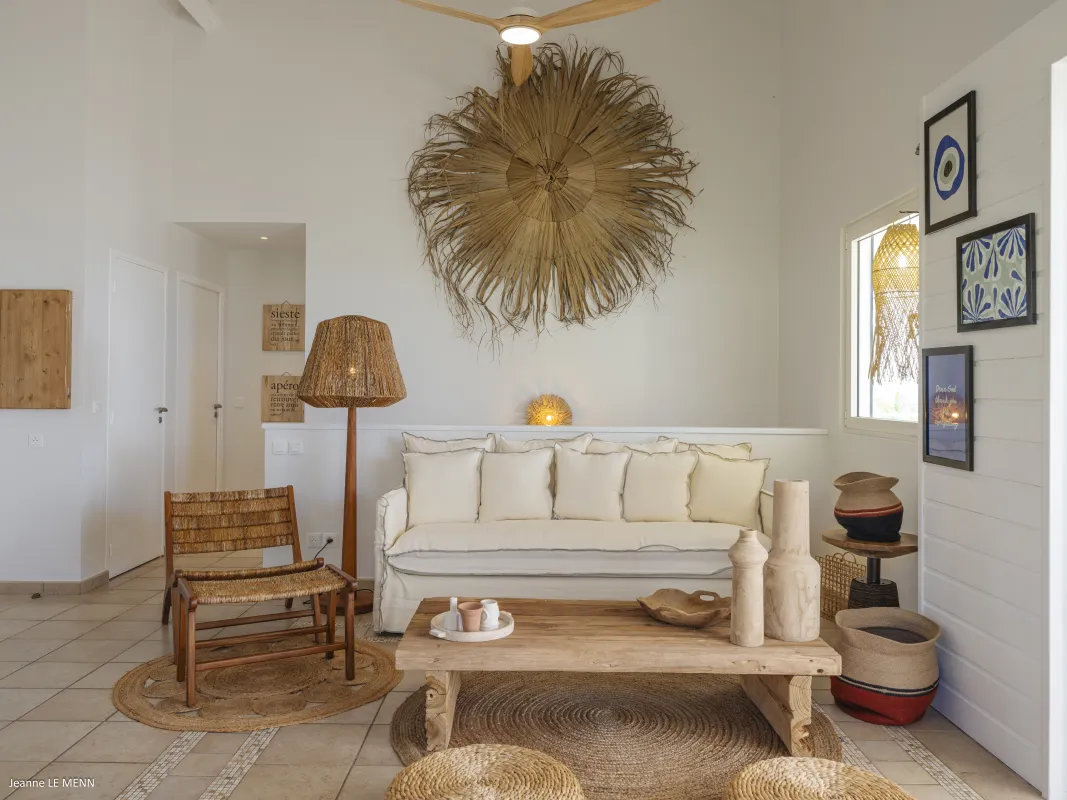 Villa Chez Paulette: Living area with white sofa, rustic wooden coffee table, woven chair, and natural straw wall decor