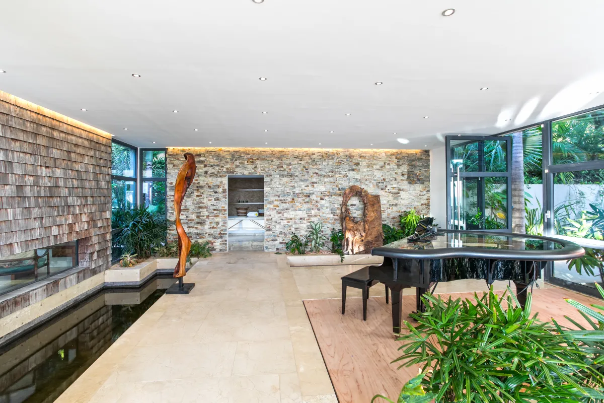 Villa Emeraude: Spacious interior area with a grand piano, indoor water feature, and wooden sculptures