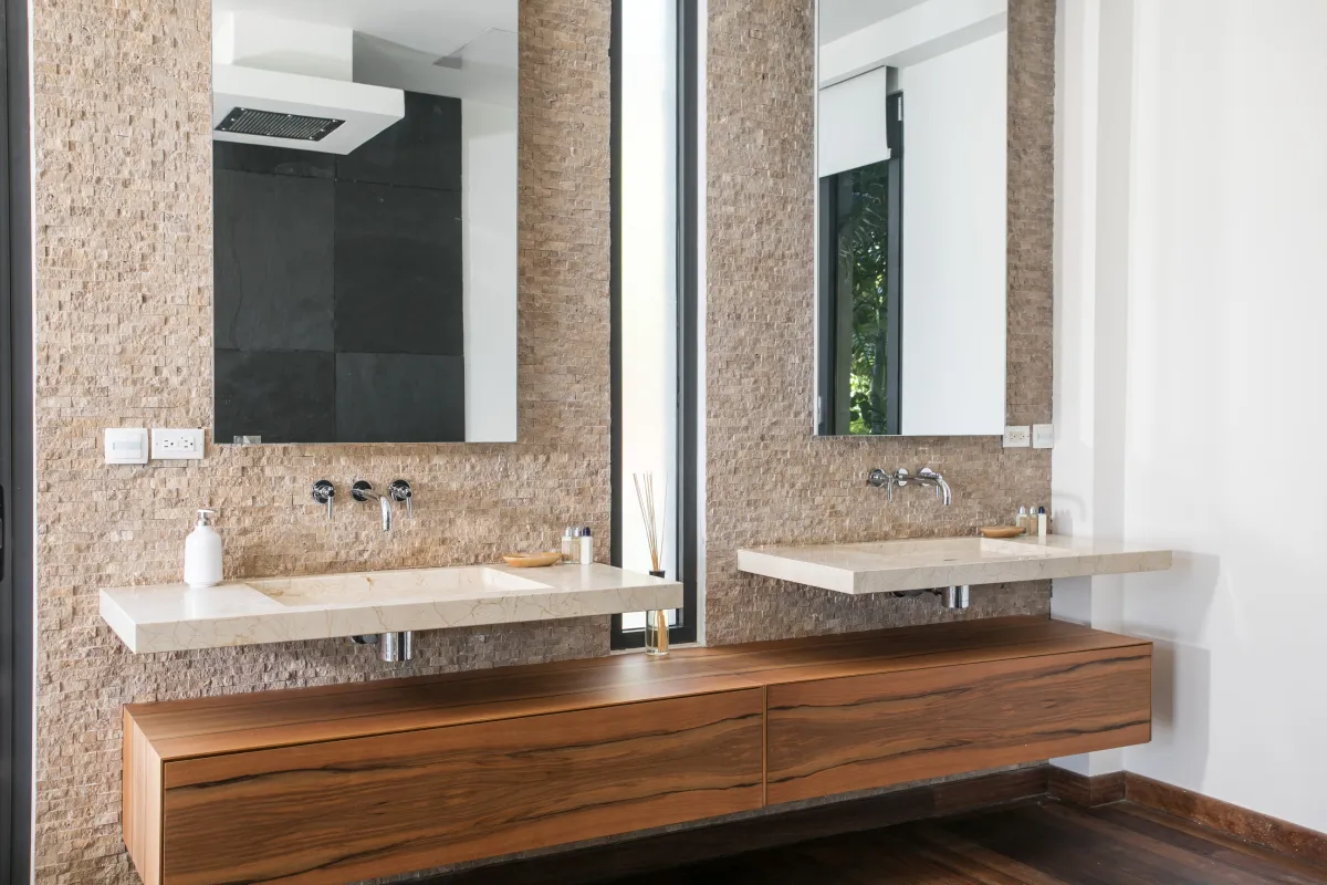 Villa Emeraude: Double vanity with floating stone sinks and wood cabinet against a textured stone wall