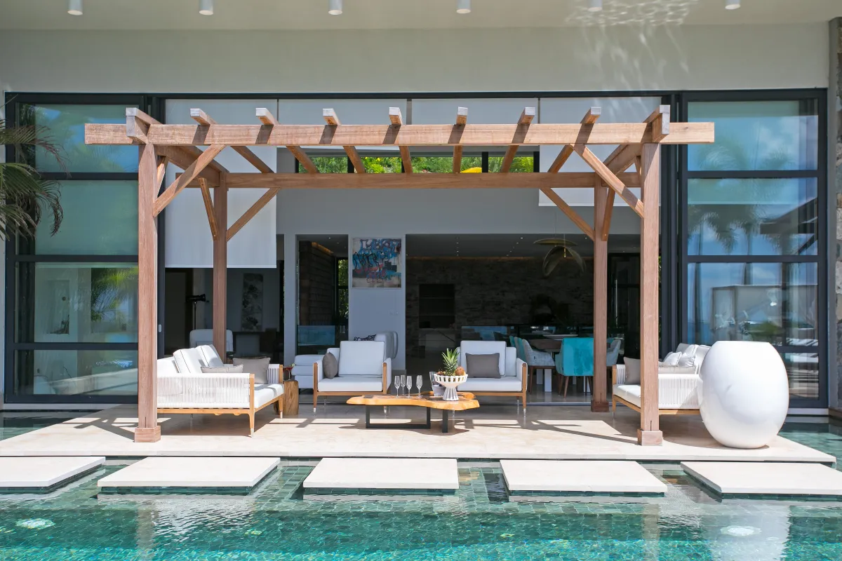 Villa Emeraude: Covered outdoor lounge with white seating under a wooden pergola next to a pool