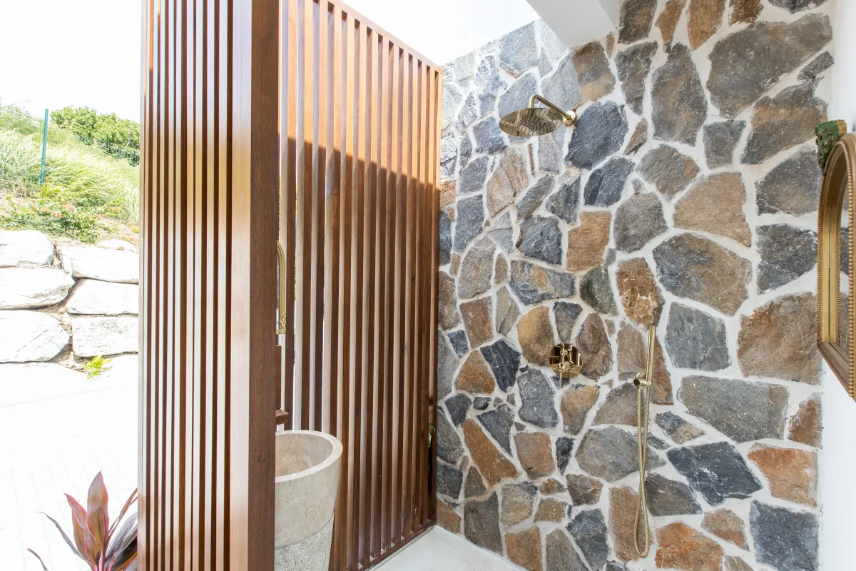 Villa Fleurs de Lys: Outdoor shower with a stone accent wall, brass fixtures, and a wooden privacy screen