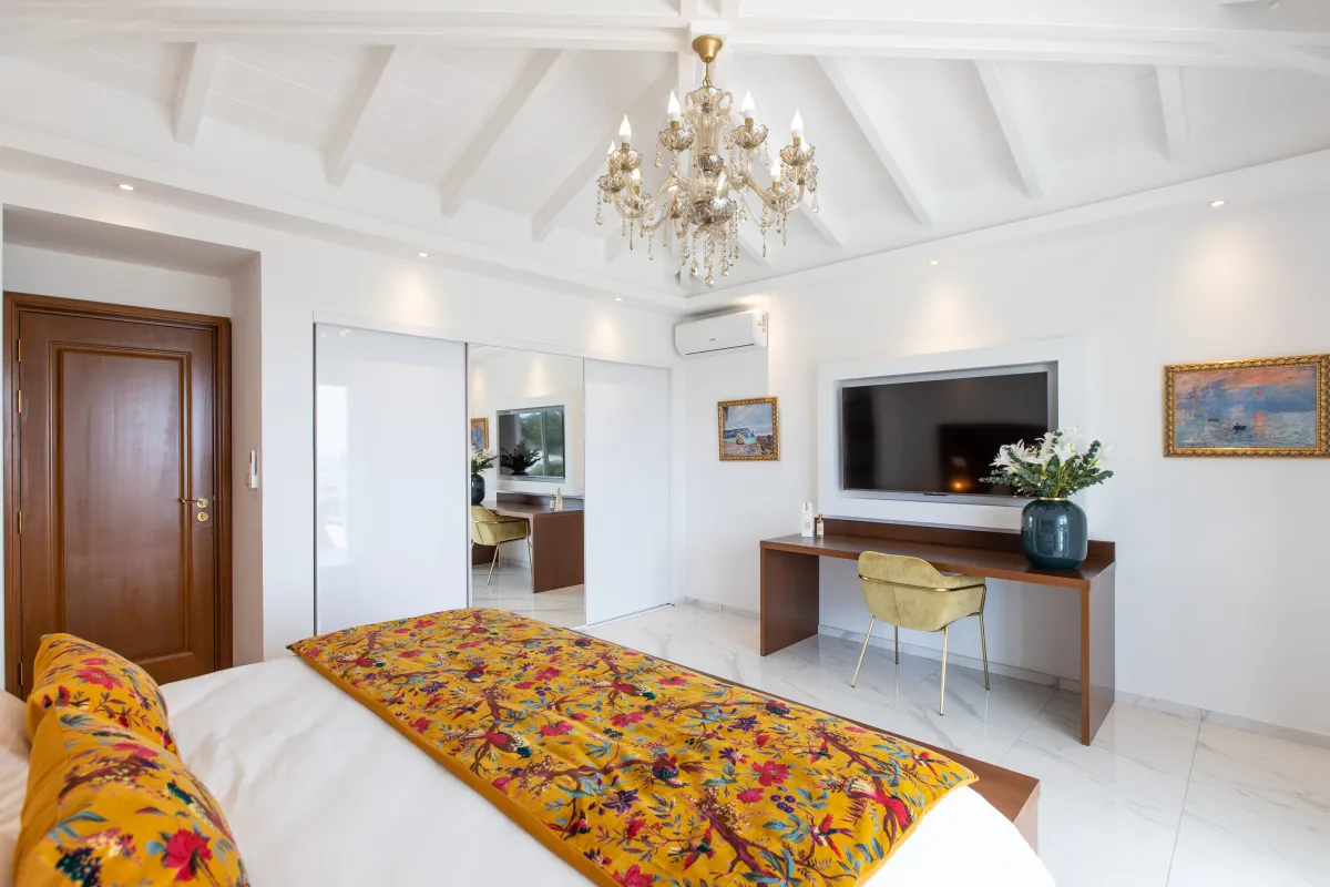 Villa Fleurs de Lys: Bedroom with vaulted beamed ceiling, chandelier, TV above desk, and patterned bedding