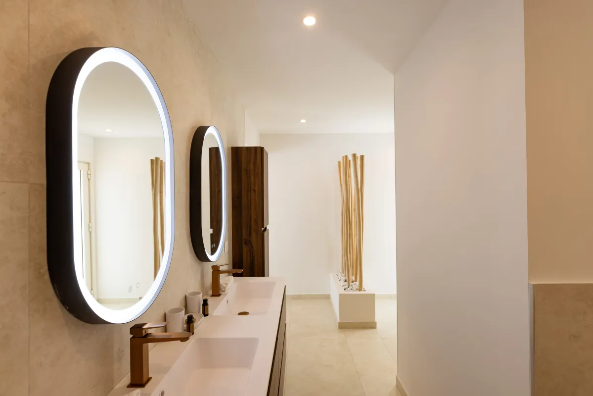 Villa Greystone: Modern bathroom vanity with double sinks bronze faucets and illuminated oval mirrors