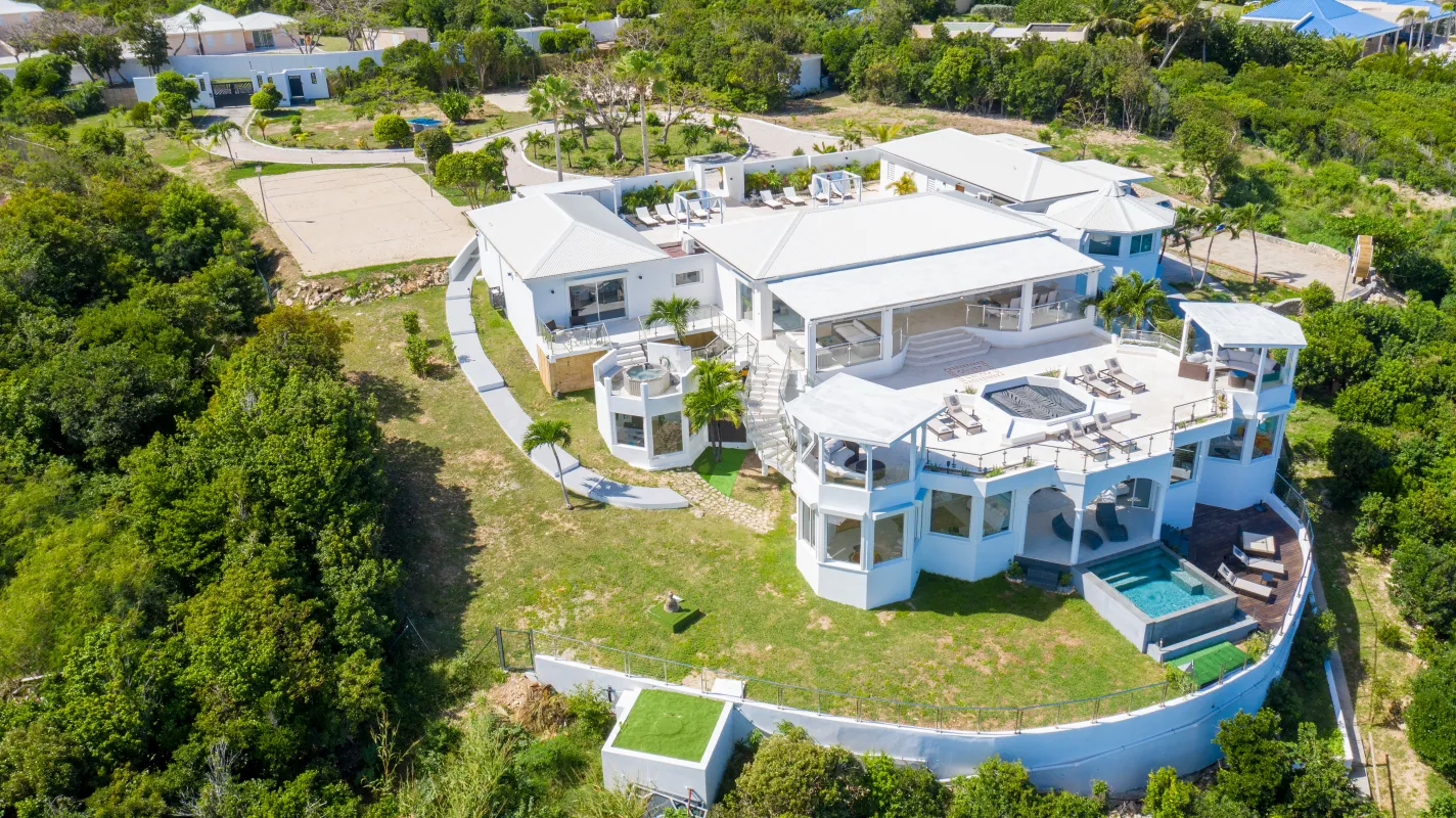 Villa Infinity Blue: Aerial view of a sprawling multi-level white villa surrounded by lush green trees