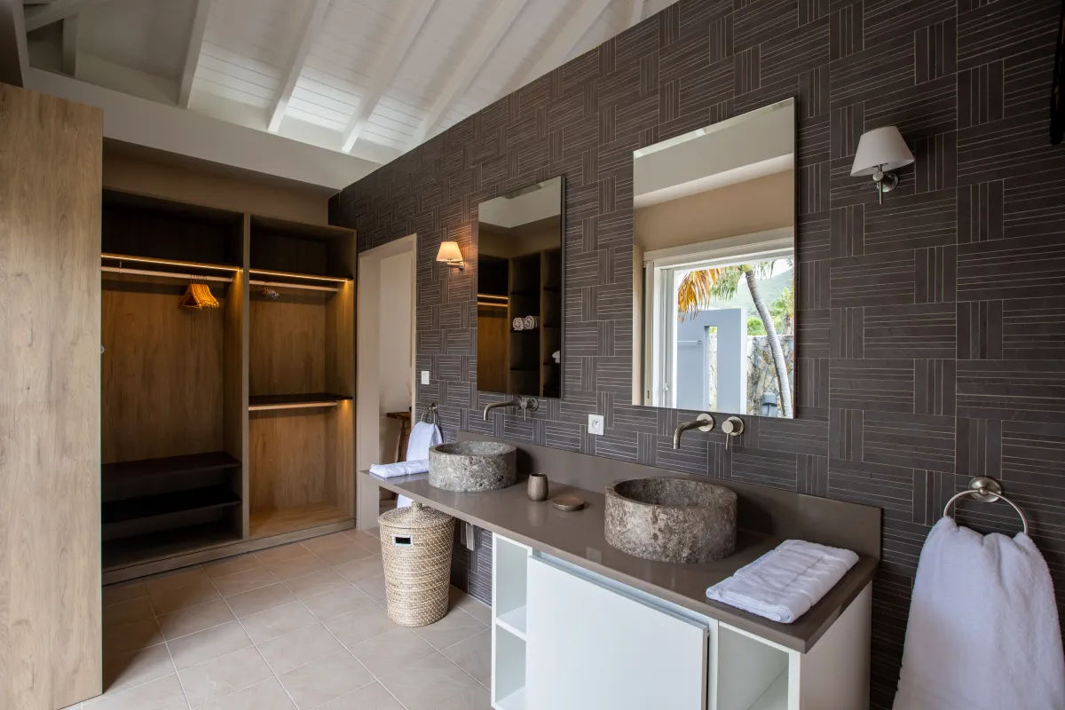Villa Karukera: Modern bathroom with double stone vessel sinks, large mirrors, and an open wooden closet