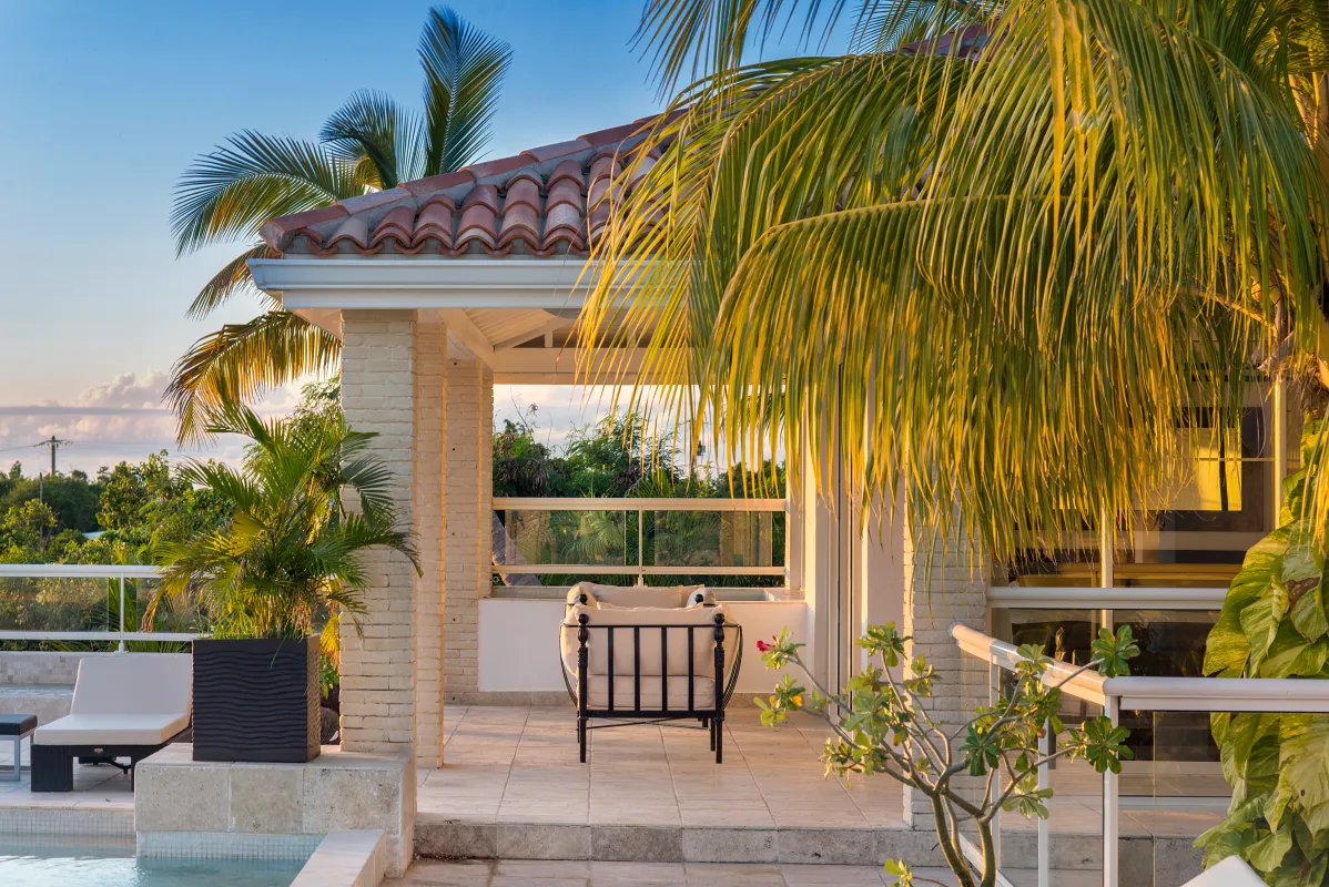 Villa La Favorita: Covered patio lounge with an armchair beside a swimming pool framed by palm leaves