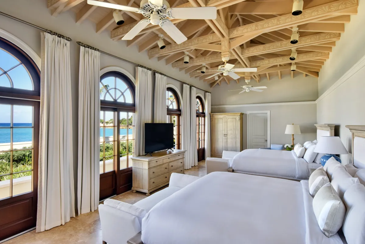 Villa Le Chateau Des Palmiers: Spacious bedroom with two beds, high exposed-beam ceilings, and arched glass doors facing the sea