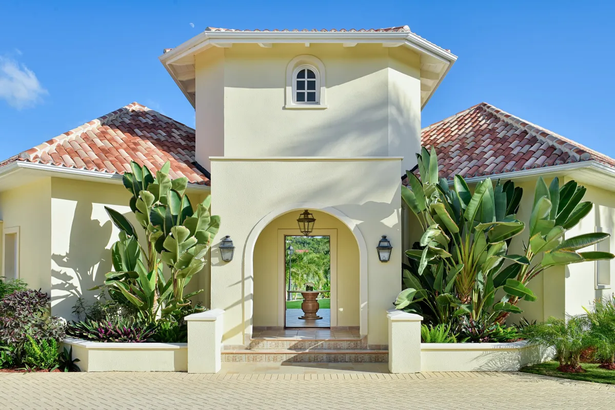 Villa Le Chateau Des Palmiers: Arched entrance to a villa framed by lush tropical foliage and clay tile roofs