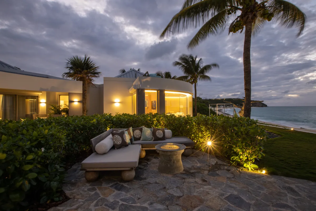Villa Le Rêve: Stone terrace with cushioned lounge seating overlooking the beach and ocean at dusk