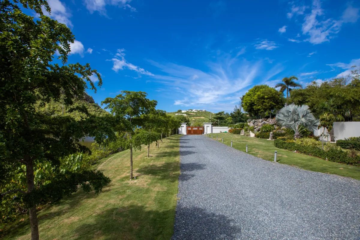 Villa Le Rêve: Gravel driveway lined with green lawns and trees leading to an entrance gate