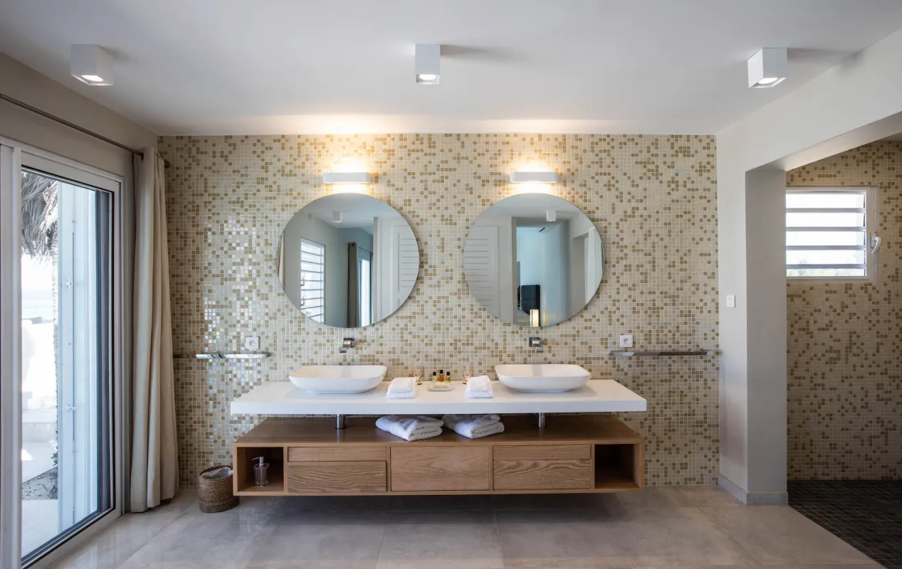 Villa L'Ecume des Jours: Modern bathroom with double vessel sink vanity, round mirrors, and mosaic tile wall