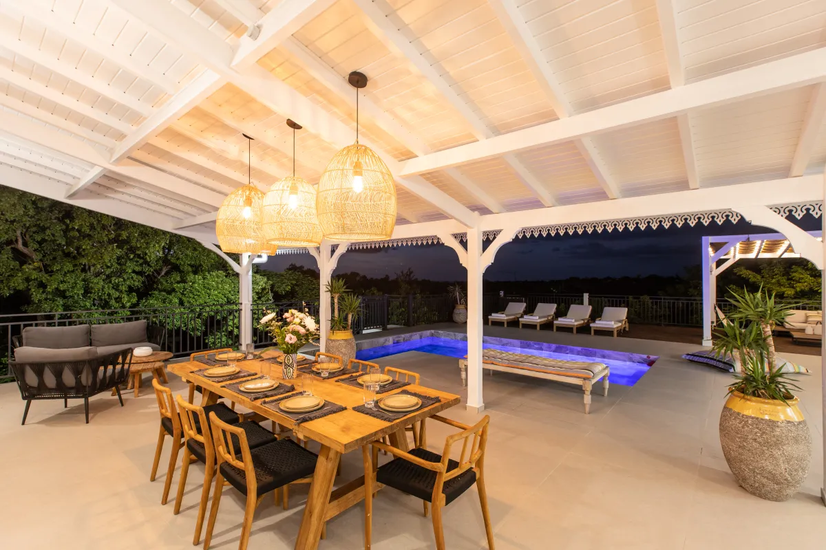 Villa Les Oliviers: Covered terrace with wooden dining table and chairs overlooking an illuminated pool at dusk