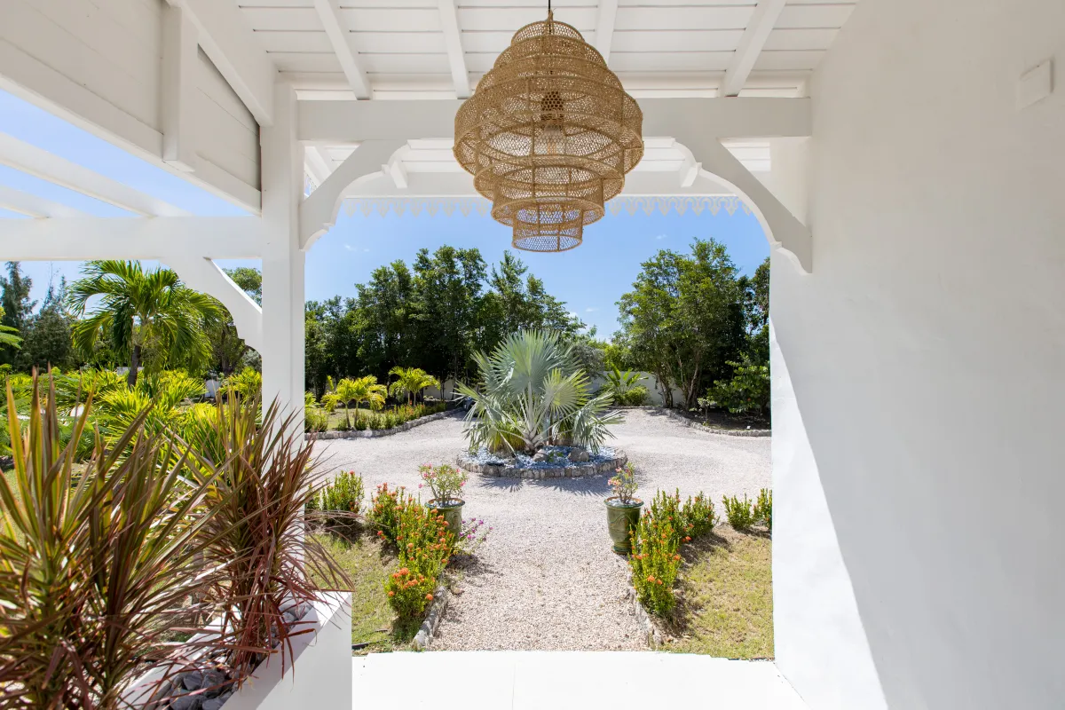 Villa Les Oliviers: View from a covered white porch with woven pendant lamp overlooking a landscaped gravel driveway