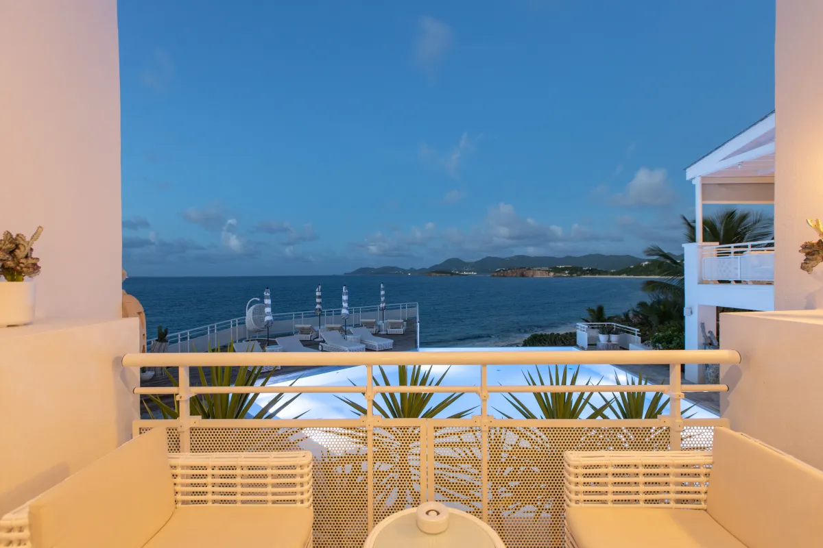 Villa L'Oasis: Balcony seating area overlooking an illuminated swimming pool and the ocean at twilight