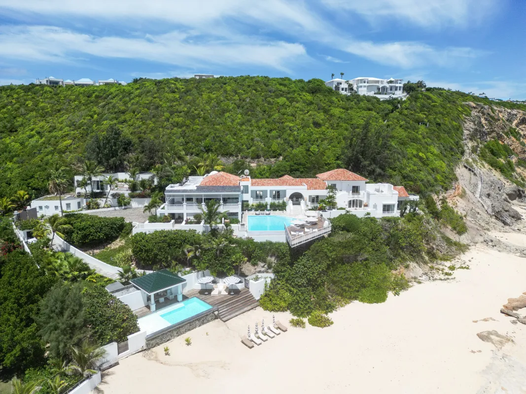 Villa L'Oasis: Aerial view of a beachfront villa estate with swimming pools against a lush green hillside