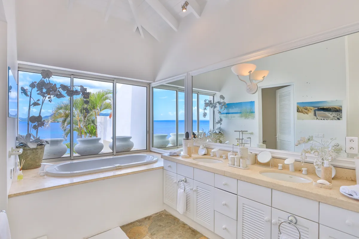 Villa L'Oasis: Bathroom with a built-in bathtub next to ocean-view windows and a double vanity
