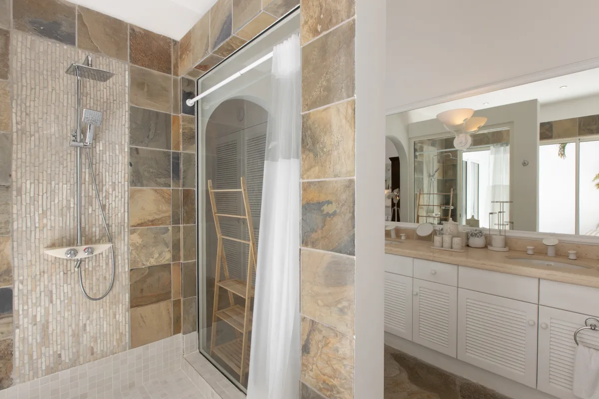 Villa L'Oasis: Walk-in shower with earthy tile and a vanity with white louvered cabinets