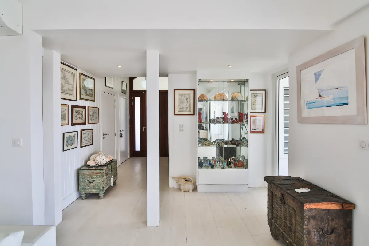 Villa Mango: White hallway decorated with antique wooden chests, framed artwork, and a glass display cabinet