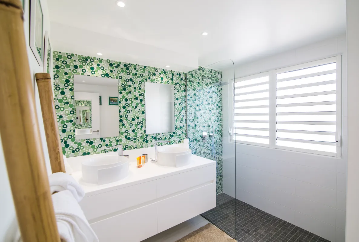 Villa Mango: Modern bathroom with double vanity, green mosaic tile accent wall, and walk-in shower