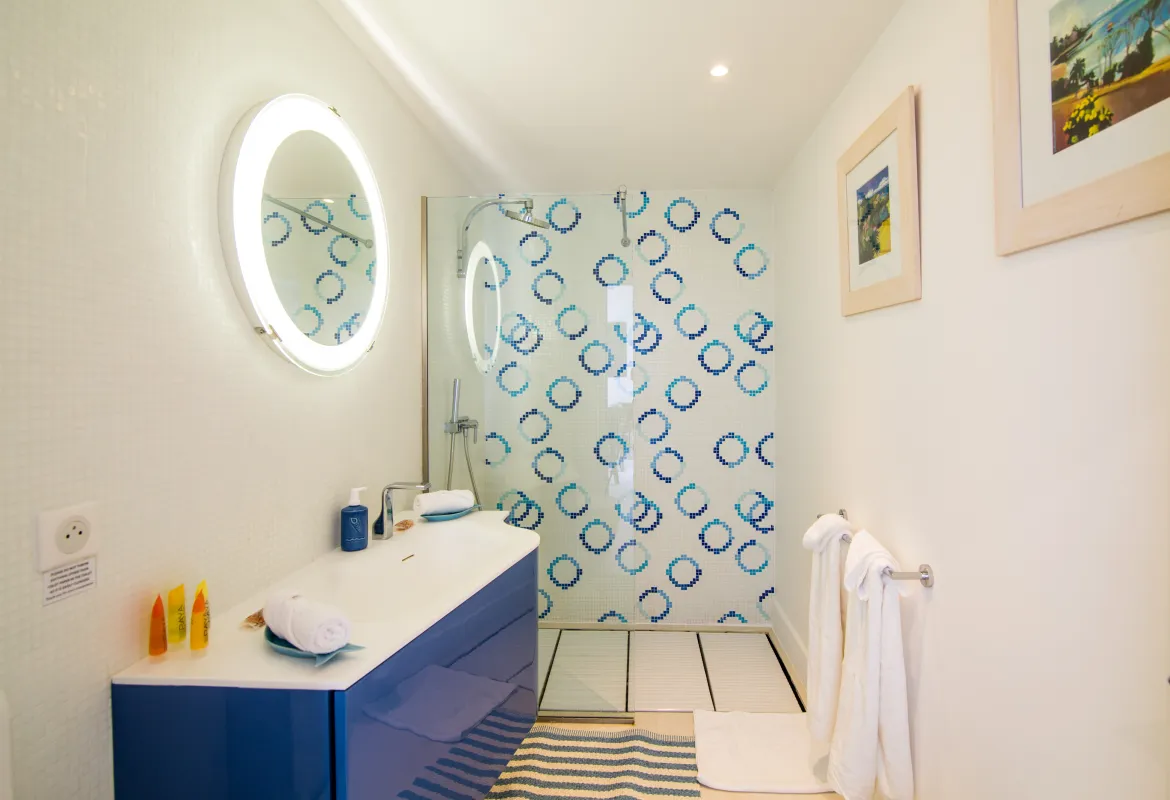 Villa Mango: Bathroom featuring a blue vanity with an illuminated mirror and patterned shower