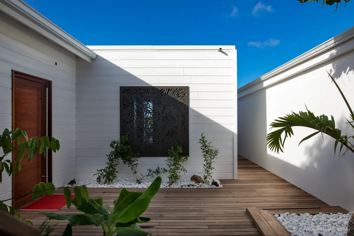 Villa Mapai: Wooden entrance deck with white exterior siding and decorative screen under clear blue sky