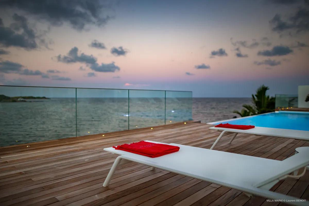 Villa Mapai: Wooden sun deck with loungers and glass railing overlooking the sea at sunset
