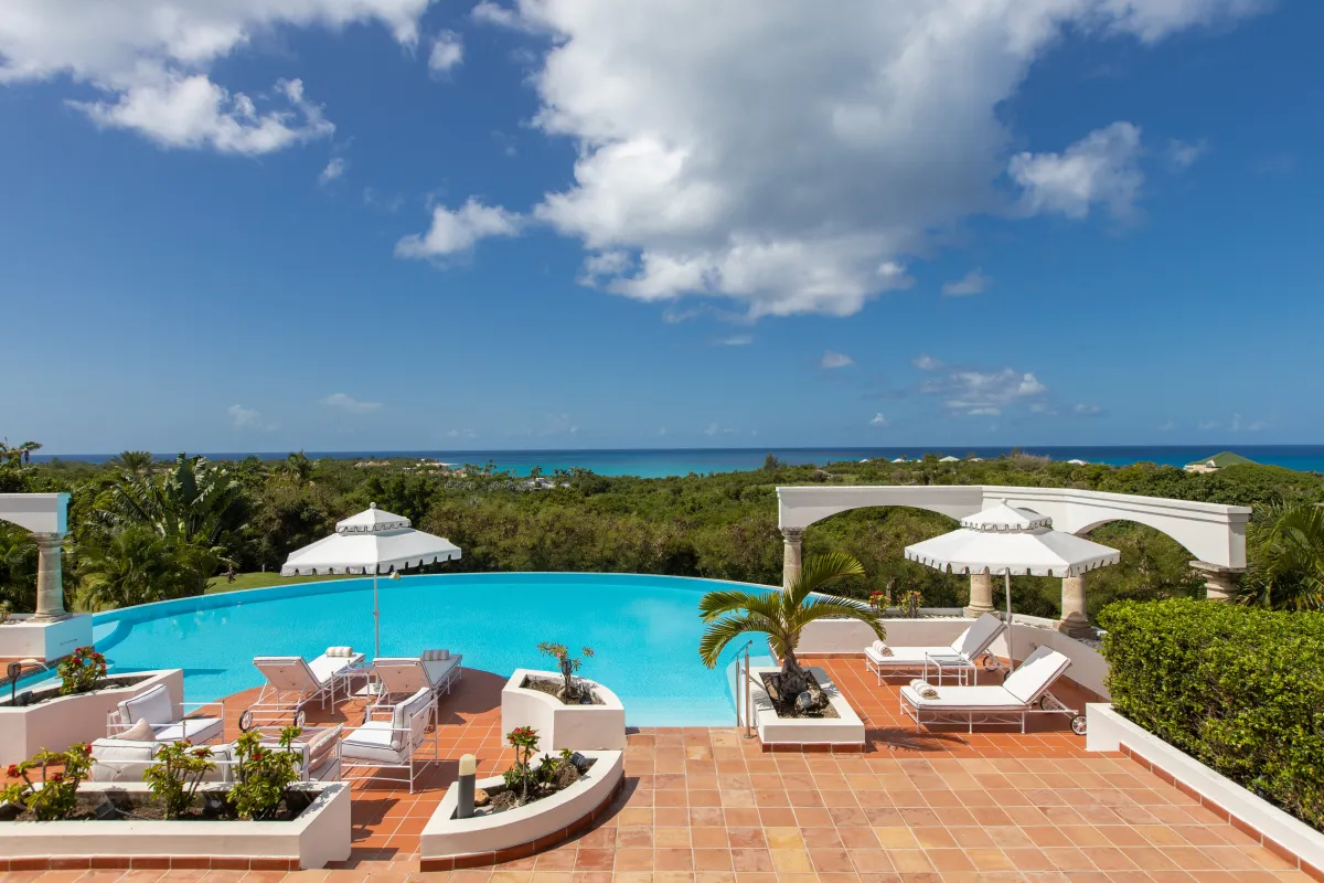 Villa Mariposa: Curved swimming pool and sun deck with lounge chairs overlooking greenery and the sea