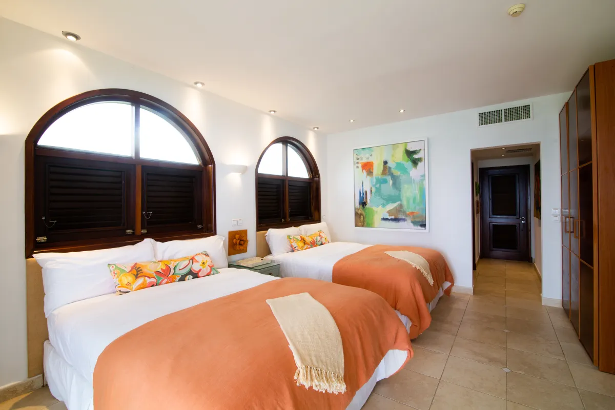 Villa Mes Amis: Bedroom with two queen beds, arched windows with dark wood shutters, and colorful artwork